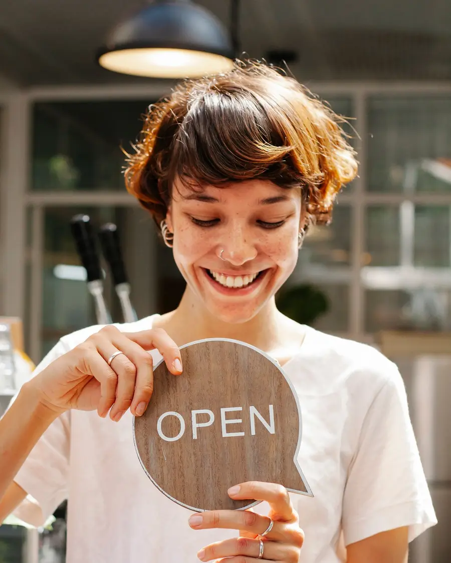 Comerciante sonriendo mientras da la vuelta al cartel de abierto de su negocio